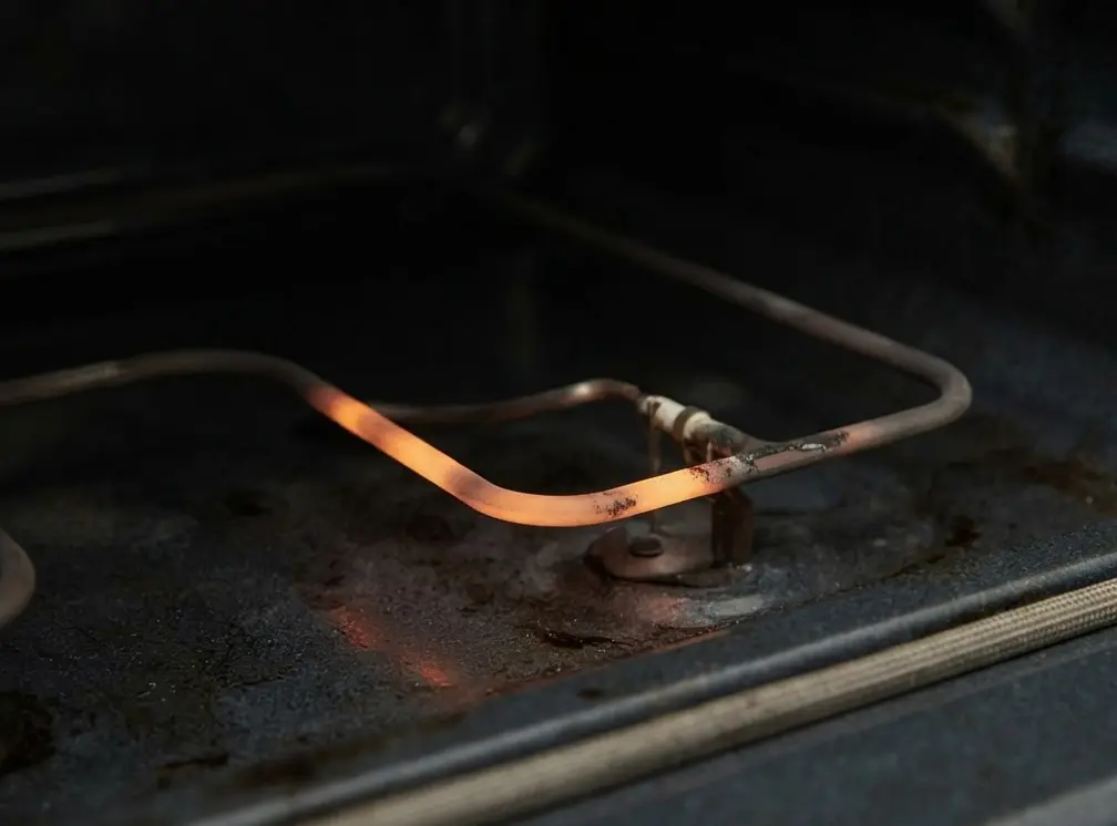 Close-up of a weak and failing gas oven igniter inside a GE range before repair.