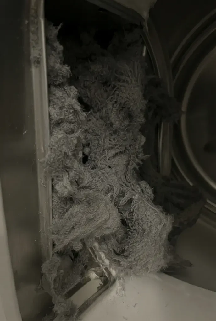 Close-up inside a dryer drum focusing on the lint filter area completely stuffed with thick grey lint.